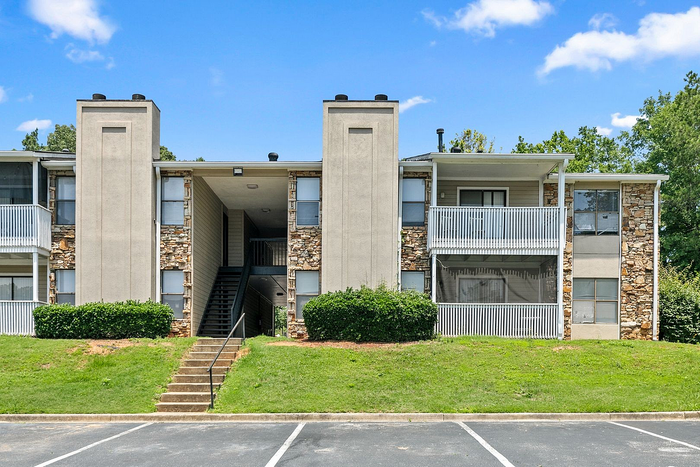 Charming apartment complex exterior with stone accents, spacious balconies, and inviting greenery under a clear blue sky.