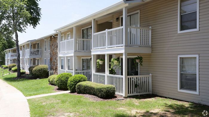 Charming apartment complex with spacious balconies, lush greenery, and inviting pathways under a clear blue sky.