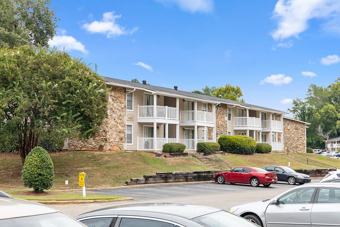 Charming apartment complex with stone accents, private balconies, and lush greenery under a clear blue sky.