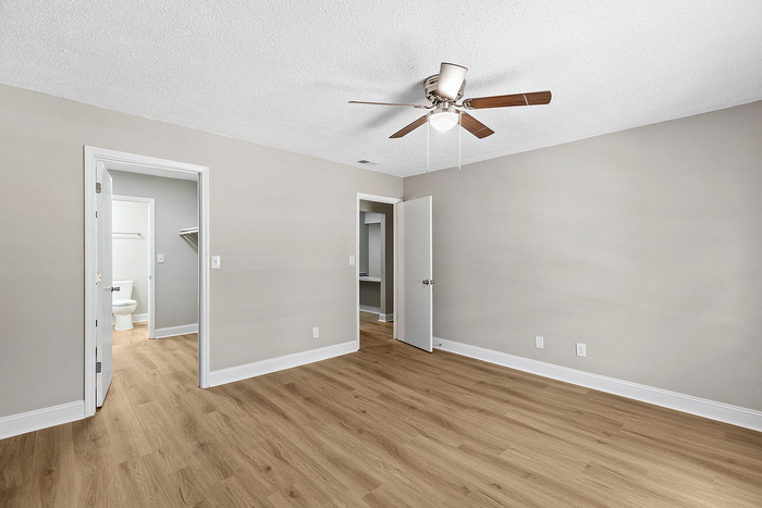 Spacious bedroom with elegant hardwood flooring, modern ceiling fan, and access to a bright en-suite bathroom.