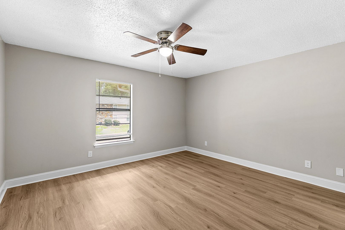 Bright and airy bedroom with sleek wooden flooring, modern ceiling fan, and a large window offering abundant natural light.