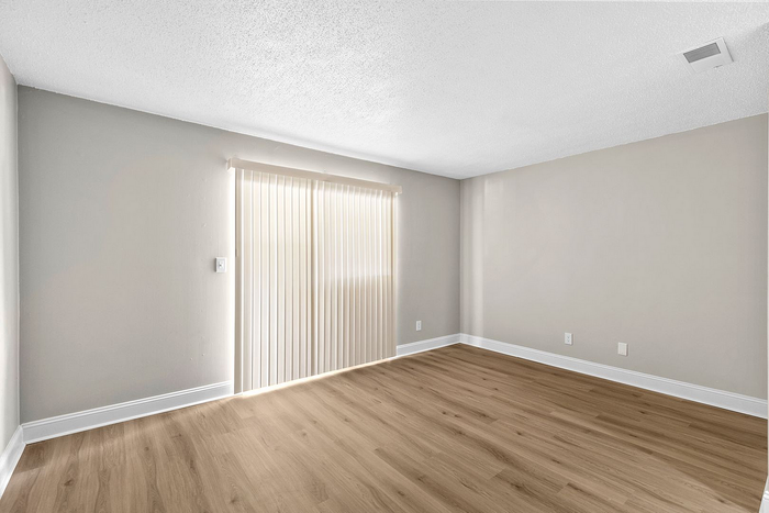Bright, minimalist room with elegant wood flooring and ample natural light through vertical blinds.