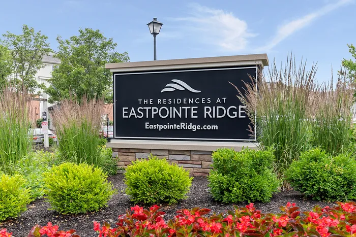 Inviting entrance sign to The Residences at Eastpointe Ridge, surrounded by vibrant landscaping and blue skies.