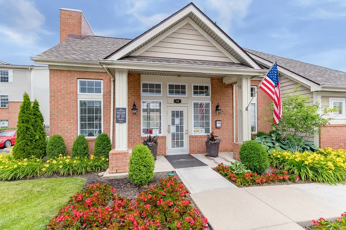 Charming brick-front apartment entrance with lush landscaping and vibrant flower beds, exuding a welcoming atmosphere.