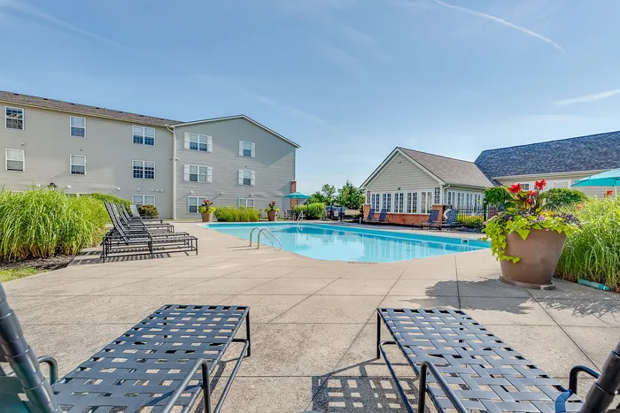 Inviting apartment complex pool with stylish lounge chairs, vibrant landscaping, and modern architecture under a clear blue sky.