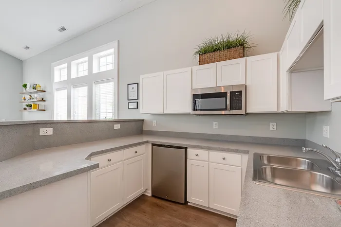 Bright and modern kitchen with sleek gray countertops, white cabinetry, and stainless steel appliances, accented by large windows offering natural light.