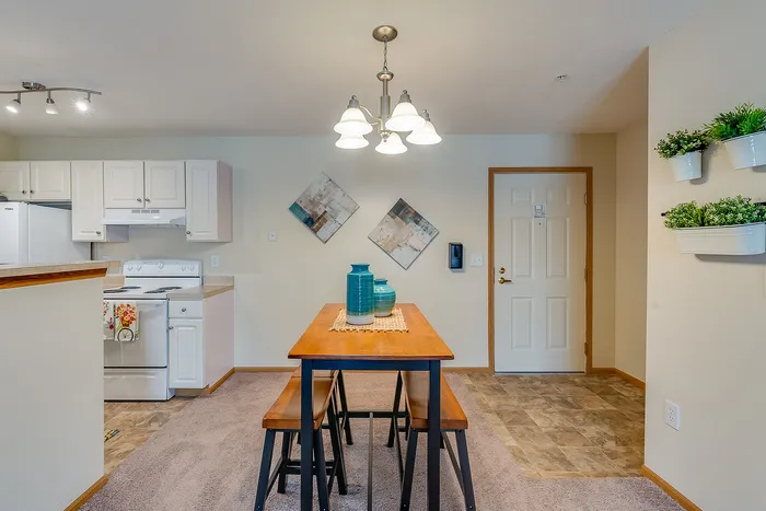 Inviting open-plan kitchen and dining area with modern lighting, wooden dining table, and wall-mounted greenery adding a cozy touch.