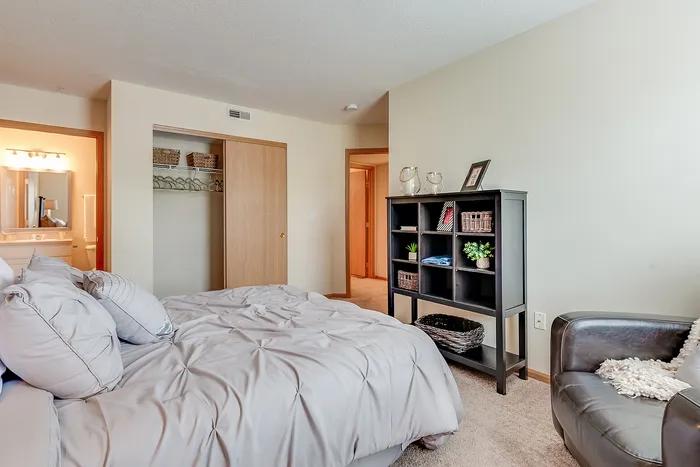 Inviting bedroom featuring a plush bed, cozy armchair, and organized shelving in a modern apartment.