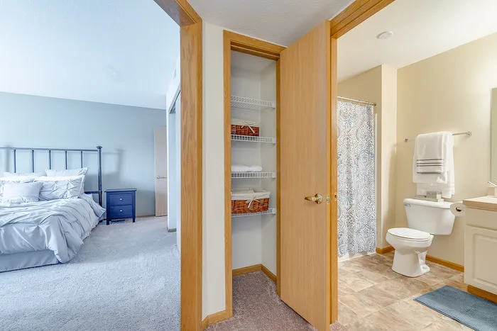 Cozy bedroom with plush carpet adjacent to a modern bathroom featuring elegant tile flooring and a chic shower curtain.