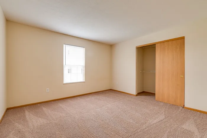 Bright, spacious bedroom with neutral walls, plush carpet, and a large closet.