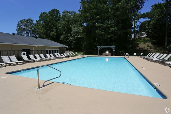 Inviting outdoor pool area with crystal-clear water, surrounded by elegant loungers and lush green trees.