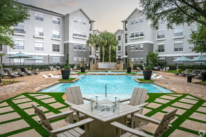 Luxurious apartment complex courtyard featuring a pristine swimming pool, elegant lounge chairs, and lush greenery, ideal for relaxation and leisure.