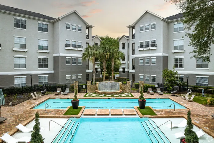 Elegant apartment complex featuring a serene outdoor pool area surrounded by lush landscaping and modern architecture.