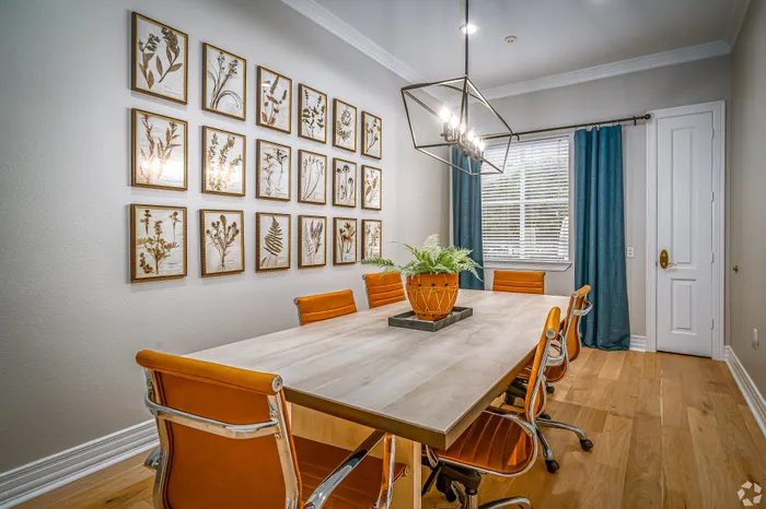 Chic dining room with a stylish wood table, vibrant orange chairs, modern chandelier, and elegant botanical wall art.