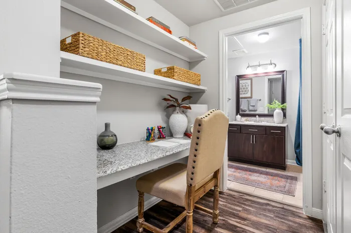 Chic and cozy home workspace with a granite desk and elegant shelving, leading to a stylish bathroom with modern fixtures.