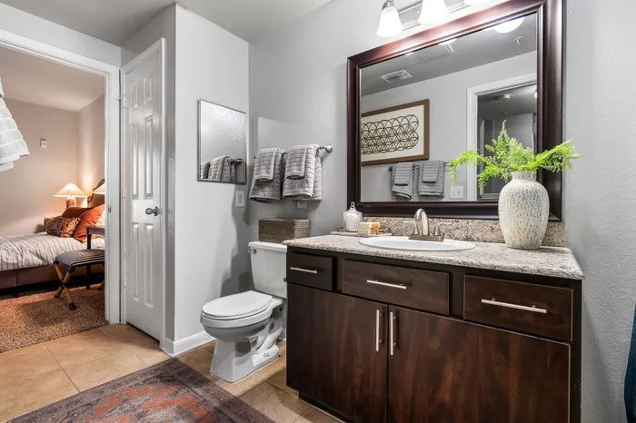 Elegant bathroom with modern fixtures, granite countertop, and a decorative vase, leading into a cozy bedroom with warm lighting.