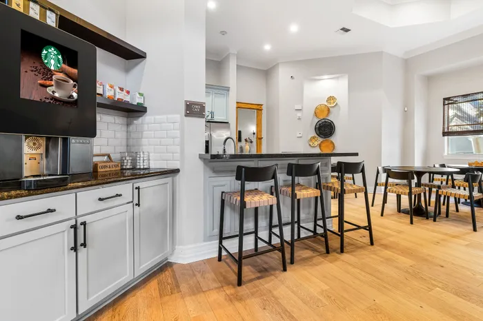 Modern kitchen and dining area featuring a sleek coffee station, elegant bar seating, and stylish decor with warm wooden flooring.