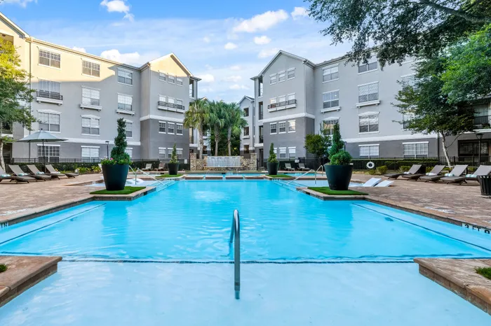 Inviting apartment complex courtyard with a luxurious swimming pool, surrounded by modern buildings and lush greenery.