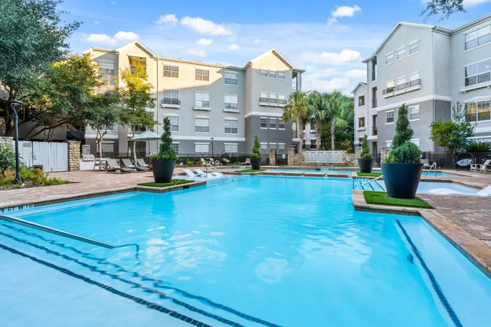 Luxurious apartment complex featuring a pristine swimming pool surrounded by lush greenery and modern architecture.