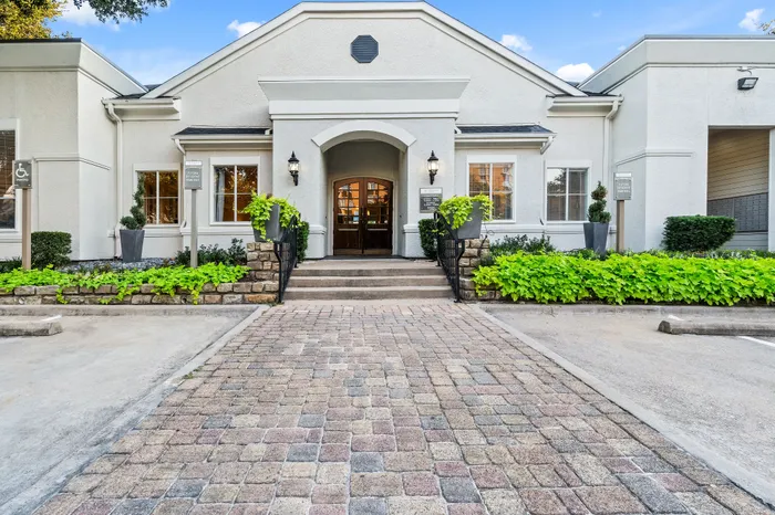 Charming apartment entrance with elegant paving, lush greenery, and welcoming double doors.