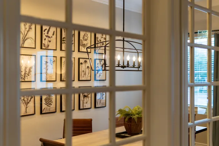 Elegant dining room view through glass doors, featuring artistic botanical wall art and chic lighting.
