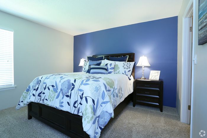Elegant bedroom with a stylish blue accent wall, cozy bed with floral bedding, and chic bedside lamps enhancing the tranquil atmosphere.