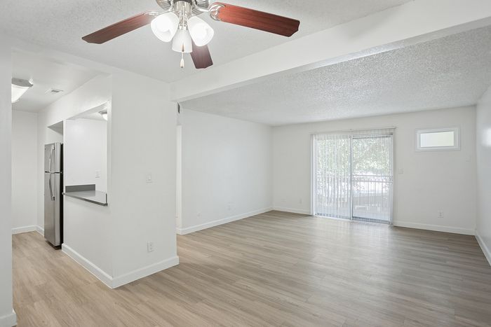 Bright and airy apartment with sleek laminate flooring, a modern ceiling fan, and large sliding glass doors leading to a balcony.