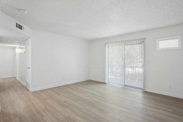 Bright and airy living space featuring elegant hardwood flooring and large sliding glass doors opening to a serene private balcony.
