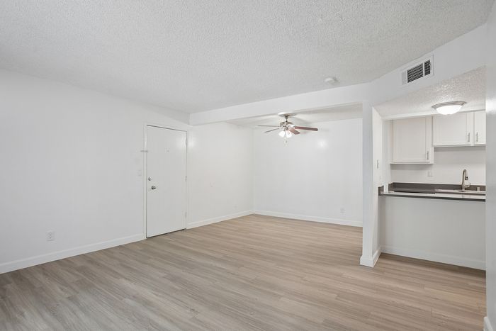 Bright and spacious open floor plan featuring modern hardwood floors, a ceiling fan, and a cozy kitchen with sleek cabinetry.