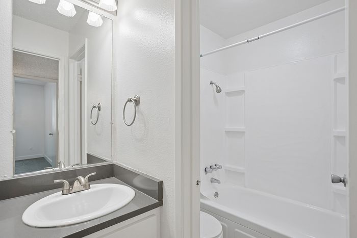 Bright, modern bathroom featuring a sleek countertop, elegant fixtures, and a spacious bathtub offering a minimalist aesthetic.