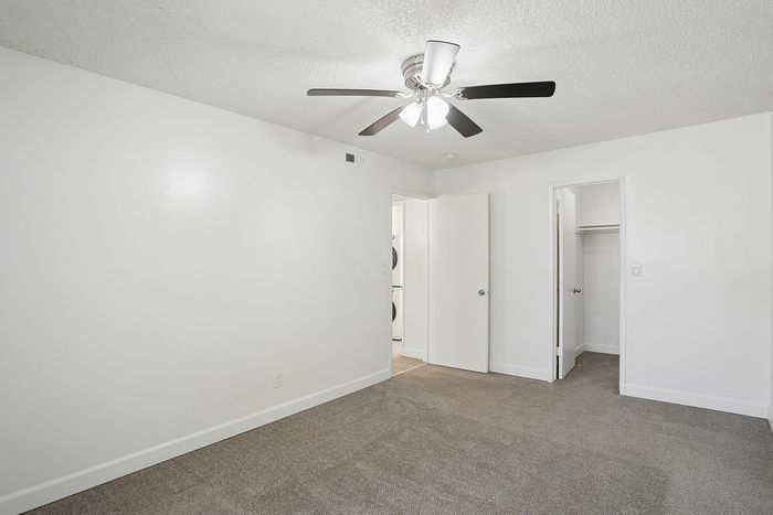 Bright and airy bedroom with plush carpet, ceiling fan, and convenient closet space.