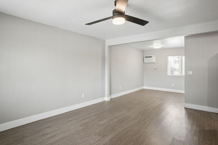 Elegant living space with sleek wooden flooring, modern ceiling fan, and abundant natural light.