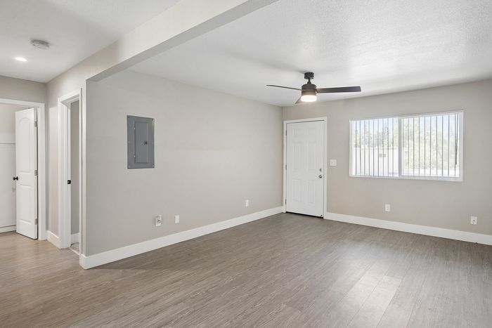 Bright and spacious room with modern wood flooring, large window, and ceiling fan, ideal for versatile living.