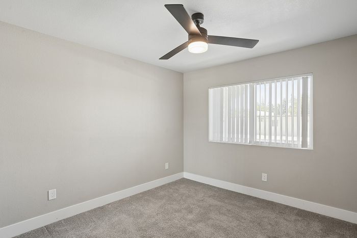 Bright, airy room with modern ceiling fan and large window allowing natural light over plush carpet.