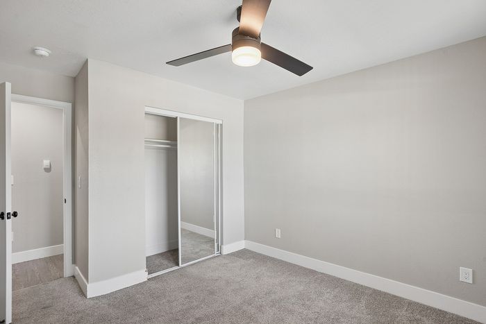 Bright and airy bedroom with plush carpeting and a modern ceiling fan, featuring a spacious mirrored closet and neutral walls.