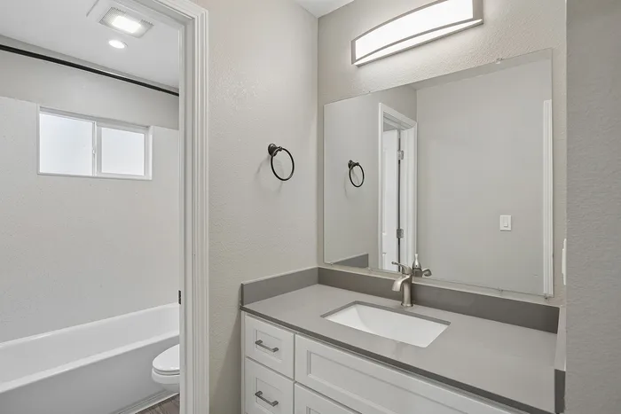 Elegant modern bathroom with sleek gray countertop, stylish vanity, and well-lit mirror.
