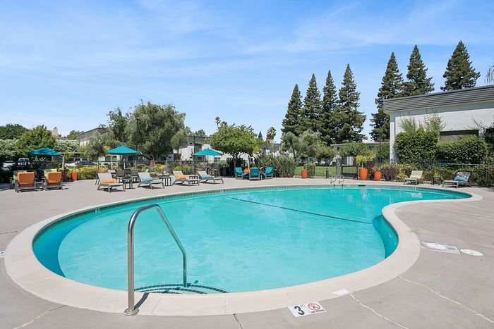 Inviting outdoor pool area with sun loungers and umbrellas, surrounded by lush greenery and clear blue skies.