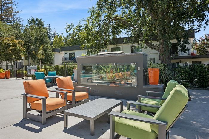 Inviting outdoor lounge area with colorful cushioned seating and a modern fire pit, perfect for relaxation and gatherings amidst lush greenery.