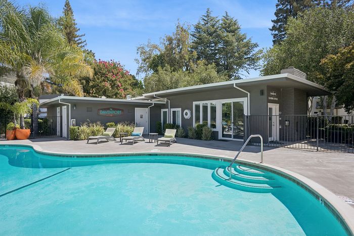Inviting poolside view of a modern apartment leasing office with lush landscaping, stylish loungers, and vibrant greenery.