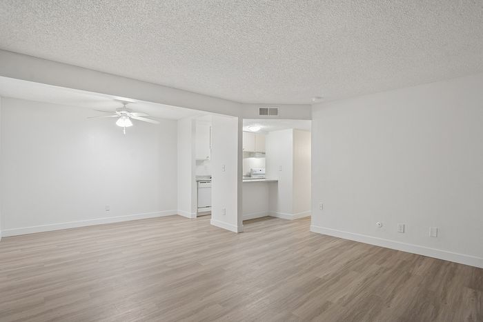 Bright and inviting open-concept living area with sleek wood flooring and ceiling fan adjacent to a cozy kitchen.