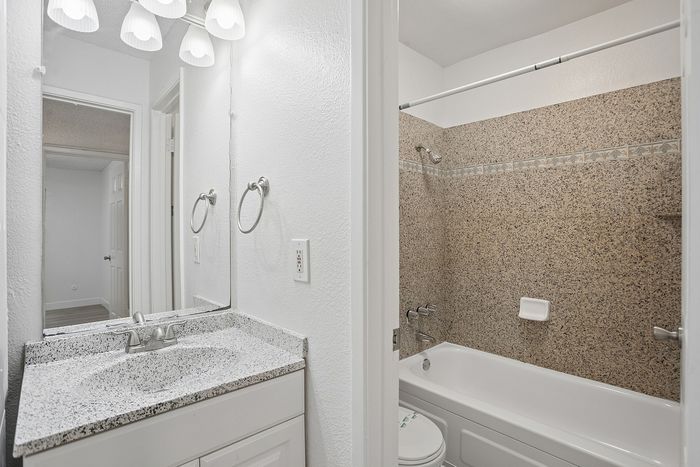 Elegant bathroom featuring a sleek granite countertop, bright vanity lighting, and a luxurious bathtub with tiled surround.