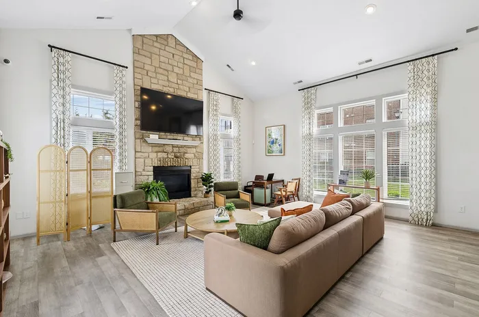 Charming living room with high ceilings, stone fireplace, plush seating, and abundant natural light from large windows.