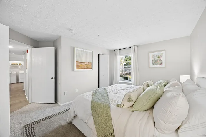 Bright and inviting bedroom with elegant decor, featuring cozy bedding, stylish artwork, and a view of the laundry room through an open door.