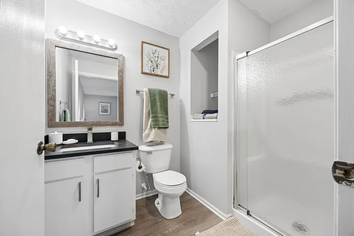 Bright and modern bathroom with elegant vanity, large mirror, and spacious glass-enclosed shower.
