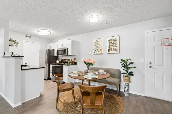 Modern kitchen and dining area with elegant decor, featuring stainless steel appliances, chic wood flooring, and a cozy dining set accentuated by natural lighting.
