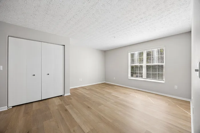 Bright and spacious bedroom with elegant hardwood flooring, a large window for natural light, and a convenient built-in closet.