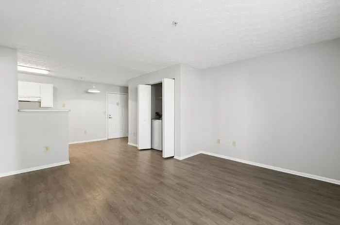 Bright and inviting open-concept apartment featuring elegant hardwood flooring, a utility closet, and modern kitchen with white cabinetry.