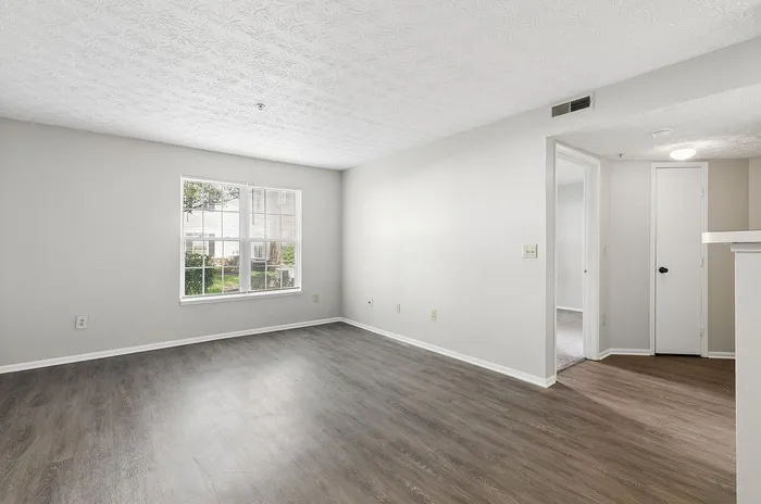 Bright and spacious apartment living area with elegant wooden flooring and large window, creating a warm and inviting atmosphere.