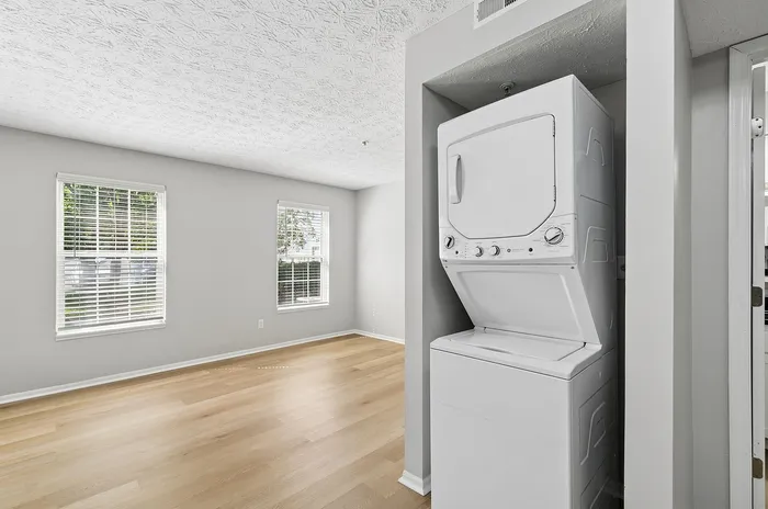 Bright living space with large windows and in-unit washer and dryer, featuring elegant light wood flooring and modern finishes.