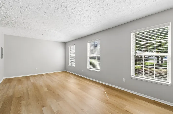Bright and airy room with elegant hardwood flooring and large windows, offering abundant natural light.